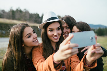 Four young women enjoying outdoors and taking selfie with cell phone. 