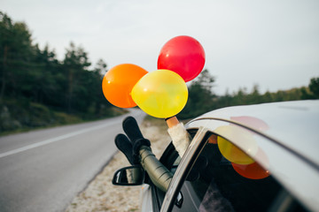 Young woman having fun while holding balloons through car window. © hedgehog94