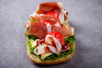 Sandwich with ciabatta, prosciutto,brie cheese and lettuce.On a grey stone background.