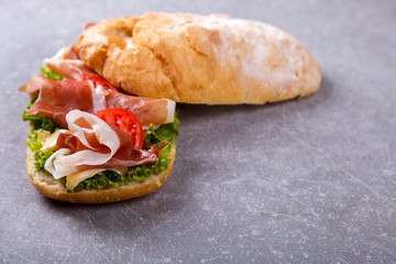 Sandwich with ciabatta, prosciutto,brie cheese and lettuce.On a grey stone background.