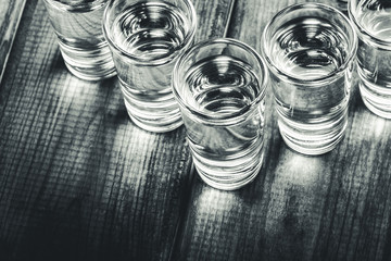 Vodka shots in a row filled with alcohol on wooden black bar.
