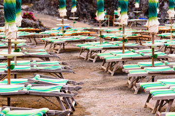 Fototapeta na wymiar Rows of closed umbrellas and deckchairs on the empty beach.