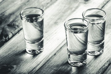 Vodka shots filled with alcohol on wooden black bar.