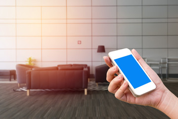 woman hand holding the phone tablet with blurred empty sofa set