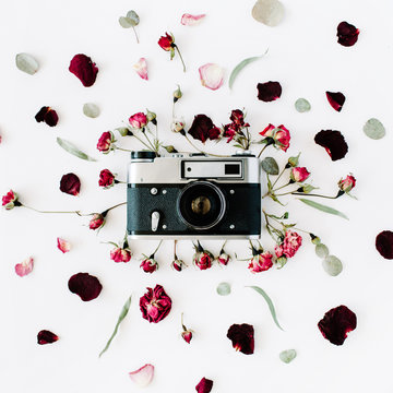 Flat lay. Vintage retro photo camera, red roses and green leaves. Top view