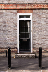Victorian black external wooden door with glass panels on a grey brick wall