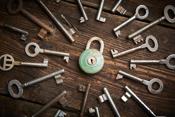 Vintage rusty padlock surrounded by old keys on a weathered steel background
