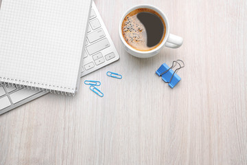 Cup of coffee with office tools on light wooden background