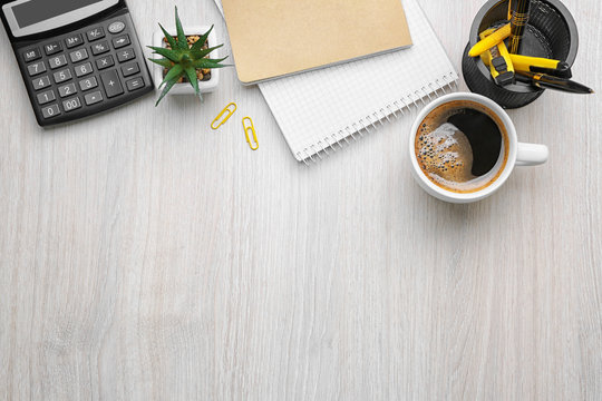 Cup of coffee with office tools on light wooden background