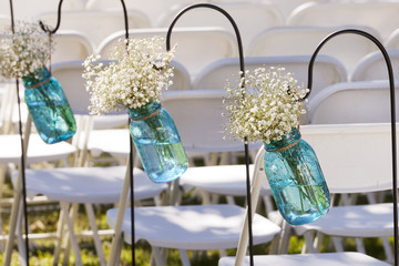 Blue vases with white flowers decorating a rustic wedding aisle 