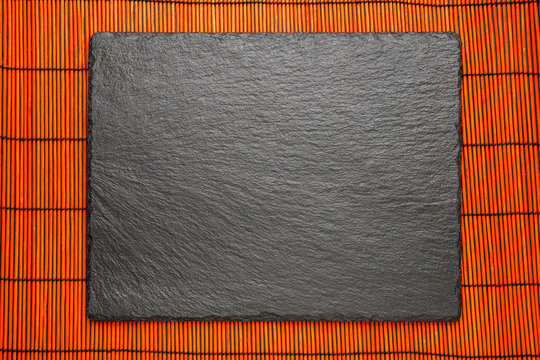 black stone plate on red bomboo mat background with copyspace, top view