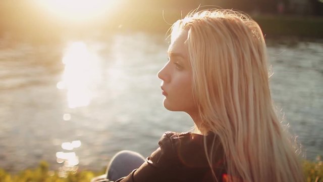 Young girl posing on the gren grass near the river at sunset