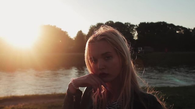 Young girl posing on the gren grass near the river at sunset