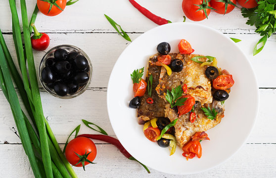 Fried hake fillet with tomato and olives in the Mediterranean style. Top view