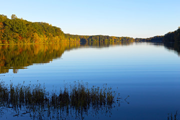 Lake fringed by colorful trees at dawn in Washington DC. Picturesque autumn foliage with reflections in the lake in North Virginia.