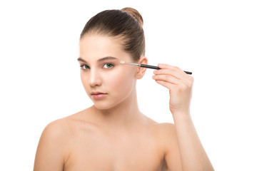 Fototapeta premium Portrait of beautiful young brunette woman with clean face. Beauty spa model girl with perfect fresh clean skin applying cosmetic brush. Youth and skin care concept. Isolated on a white background.