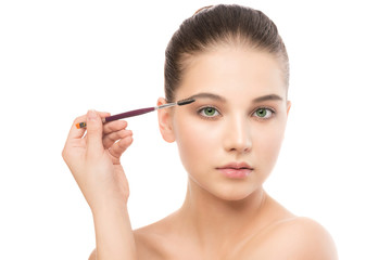 Fototapeta premium Portrait of beautiful young brunette woman with clean face. Beauty spa model girl with perfect fresh clean skin applying cosmetic brush. Youth and skin care concept. Isolated on a white background.