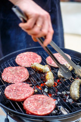 Burgers and sausages for hot dogs are roasting on the grill.