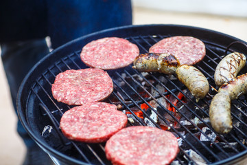 Burgers and sausages for hot dogs are roasting on the grill.