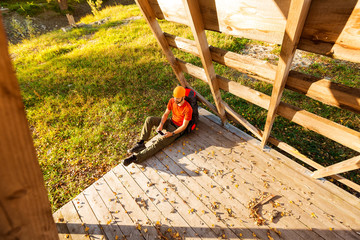 Young male traveling, resting in countryside sitting in hut, with tourist rucksack, using smartphone while enjoying nature view and summer rest