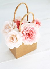 Obraz na płótnie Canvas Fresh delicate roses in craft paper shopping bag. Pretty simple gift. Soft focus. 