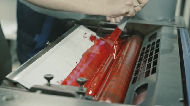 Worker at Polygraphy printing industry use Red paint on ink roller, close up