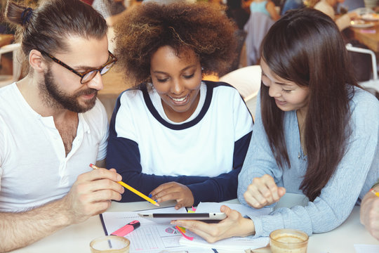 Brainstorm concept. Young colleagues of diverse ethnicities working together on common project, analyzing financial statistics and company's growth, making report at cafeteria, using touch pad pc