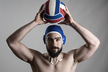 Happy professional water polo player holding ball over his head looking at camera over gray studio...