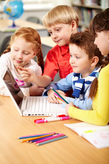 Four schoolchildren sitting in classroom and watching something on a laptop