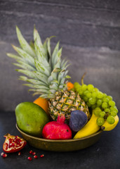 Fresh and ripe tropical fruits in old plate on dark stone background. Still life. 