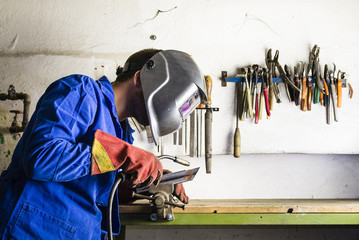 Handyman welding steel in his garage with helmet and safety gloves