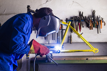 Handyman welding steel bicycle frame with helmet and safety gloves - bike frame building