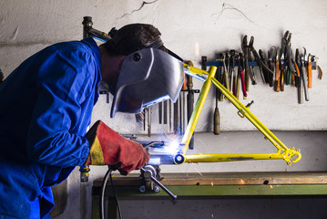Handyman welding steel bicycle frame with helmet and safety gloves - bike frame building