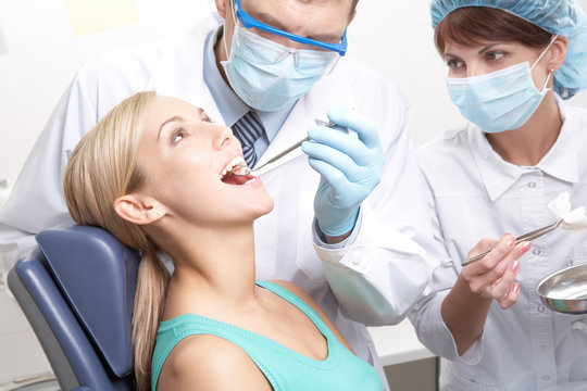 Two dentists examining a young woman s teeth