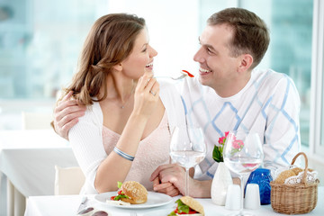 A young girl sitting with her boyfriend in cafe and feeding him with a fork