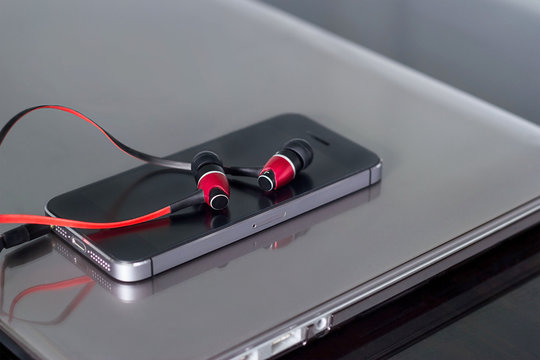 Red earphones and mobile phone on laptop background
