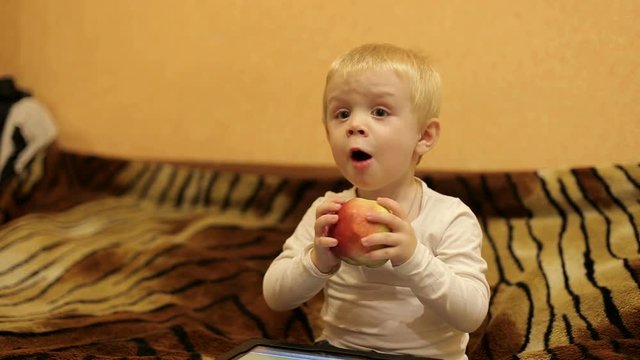 Cute little baby eating a big red Apple and watching TV.