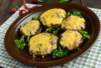 Stuffed mushrooms with salami and mozzarella cheese in a clay bowl on a wooden background.
