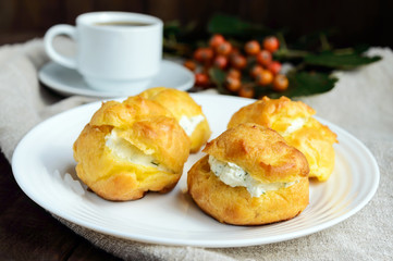 Freshly baked buns eclairs stuffed with spicy cottage cheese and a cup of coffee (espresso) on a dark wooden background. Light breakfast.