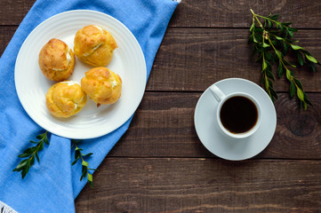 Freshly baked buns eclairs stuffed with spicy cottage cheese and a cup of coffee (espresso) on a dark wooden background. Light breakfast. The top view