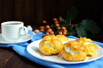 Freshly baked buns eclairs stuffed with spicy cottage cheese and a cup of coffee (espresso) on a dark wooden background. Light breakfast. 