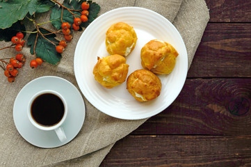 Freshly baked buns eclairs stuffed with spicy cottage cheese and a cup of coffee (espresso) on a dark wooden background. Light breakfast. The top view