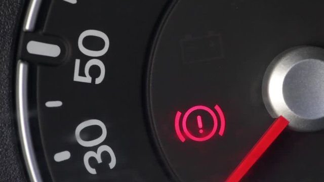 Close up footage of a car's parking brake light coming on, on the dashboard.
