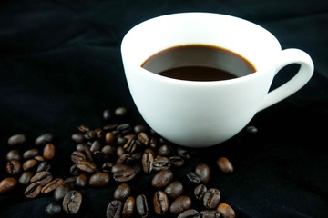 A cup of coffee and coffee beans. Black background.