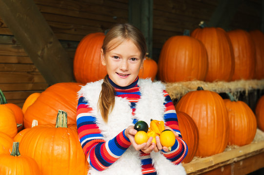 Adorable little girl of 8-9 year old choosing halloween pumpkin on farm market