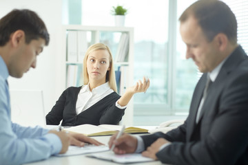 Young serious businesswoman communicating in office with her colleagues 