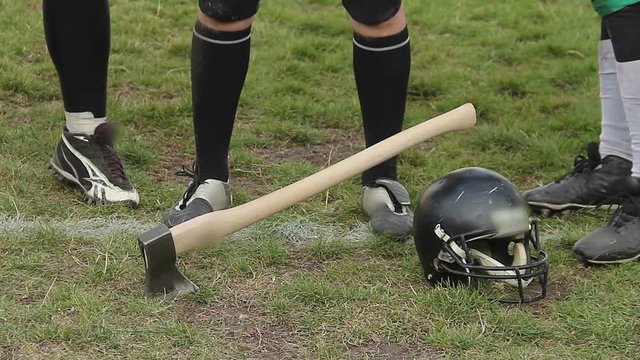 Axe stuck in gridiron field grass, football players ready to compete for trophy