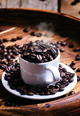 Grains of roasted coffee in a white cup, vintage wooden backgrou