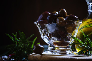 Greek olives in a glass bowl and oils, dark wood background, sel