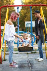 Fototapeta na wymiar Mom with pink hair whirls her little daughter on the swing